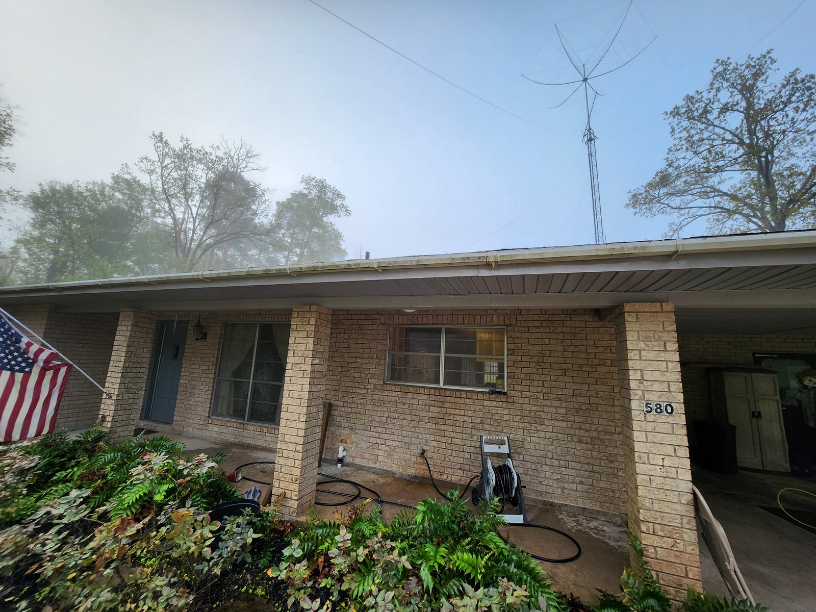 Brick home with American flag before soft washing — algae and mildew staining visible